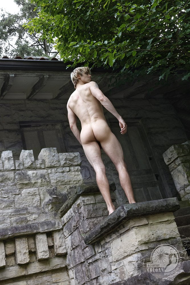 nude man standing on stone wall in front of old building