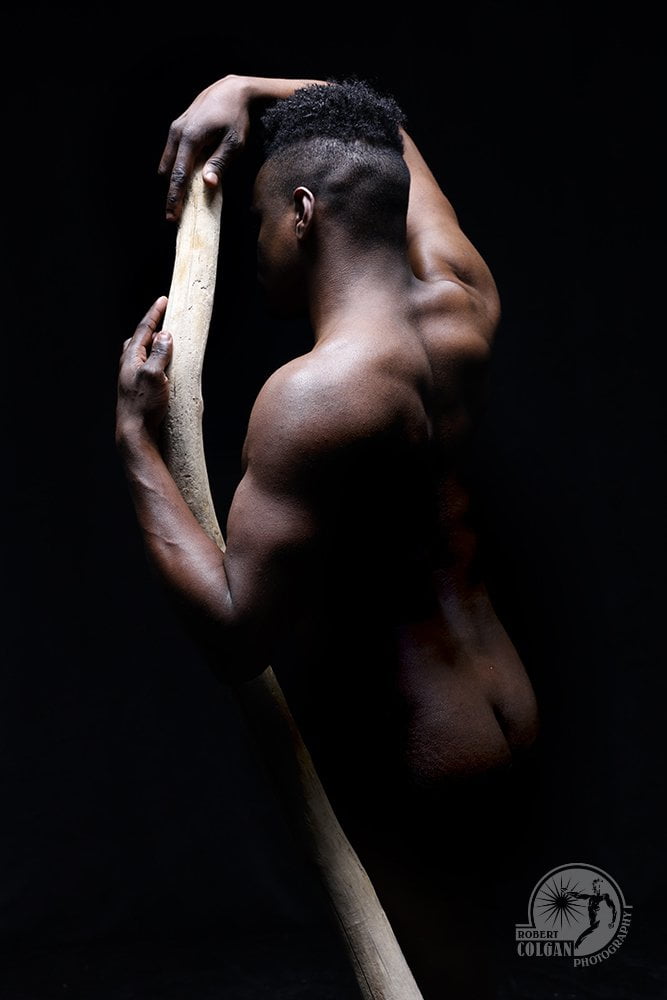 nude man with back to camera holding driftwood