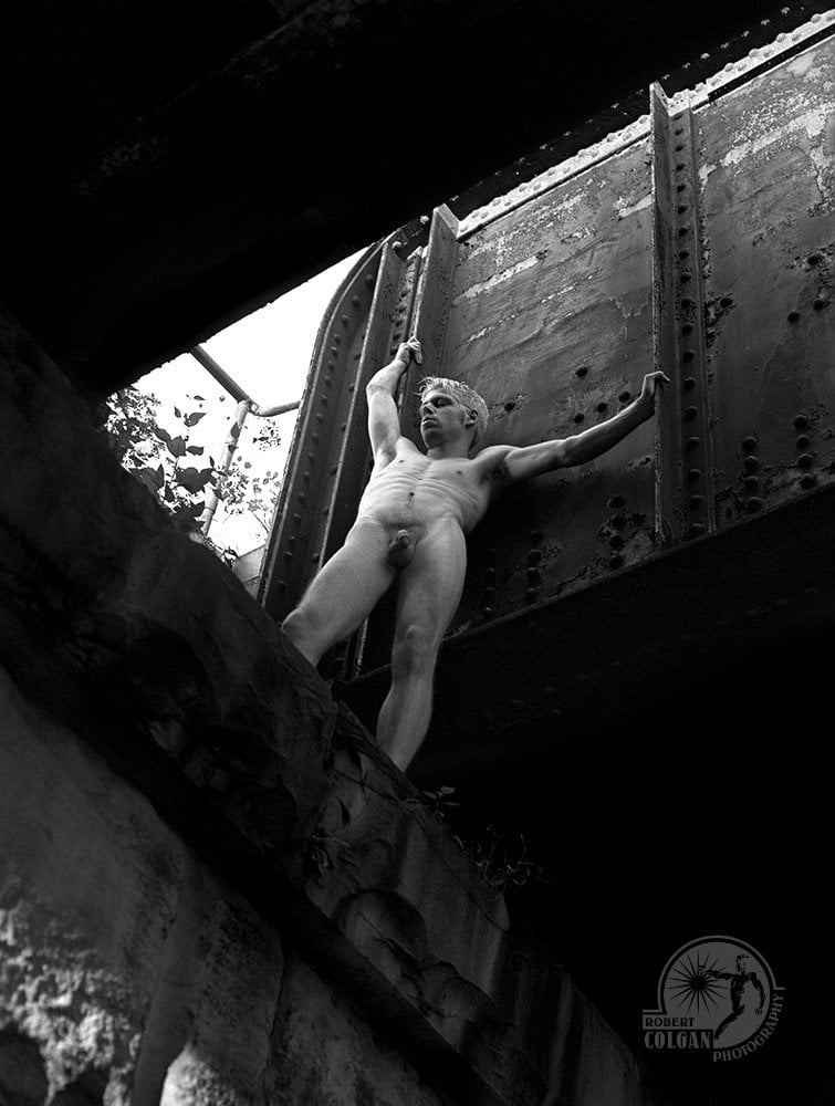 nude man standing beside iron structure, shot from below
