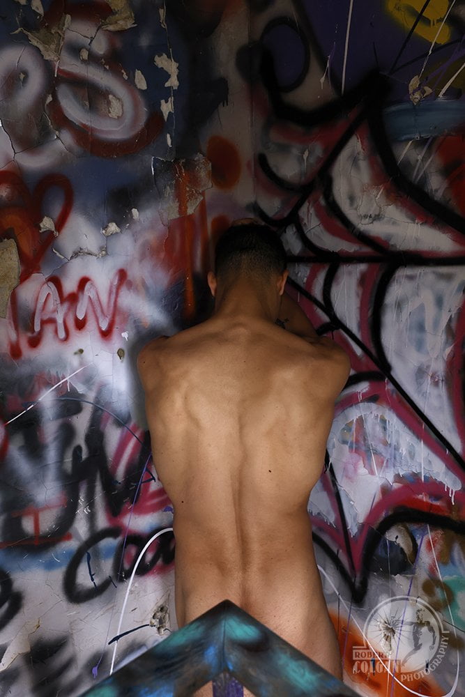 nude man facing into corner with lots of graffiti