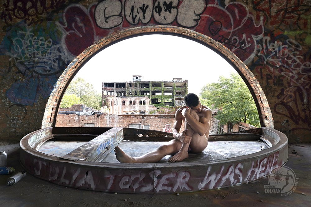 nude man curled up in remains of arched window
