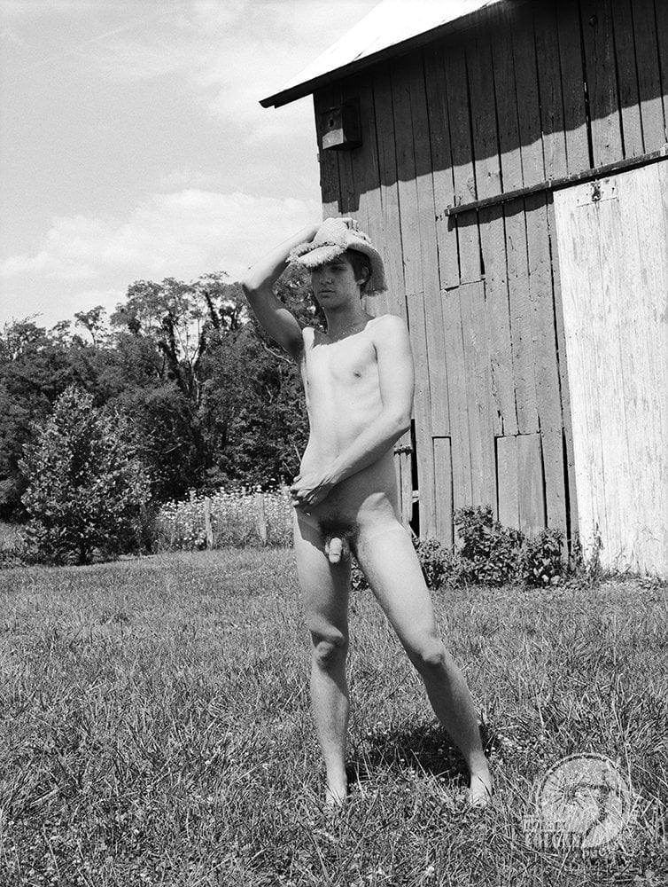 nude man in straw hat in front of barn