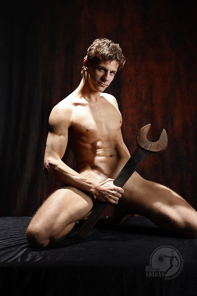 nude man seated, holding large wrench