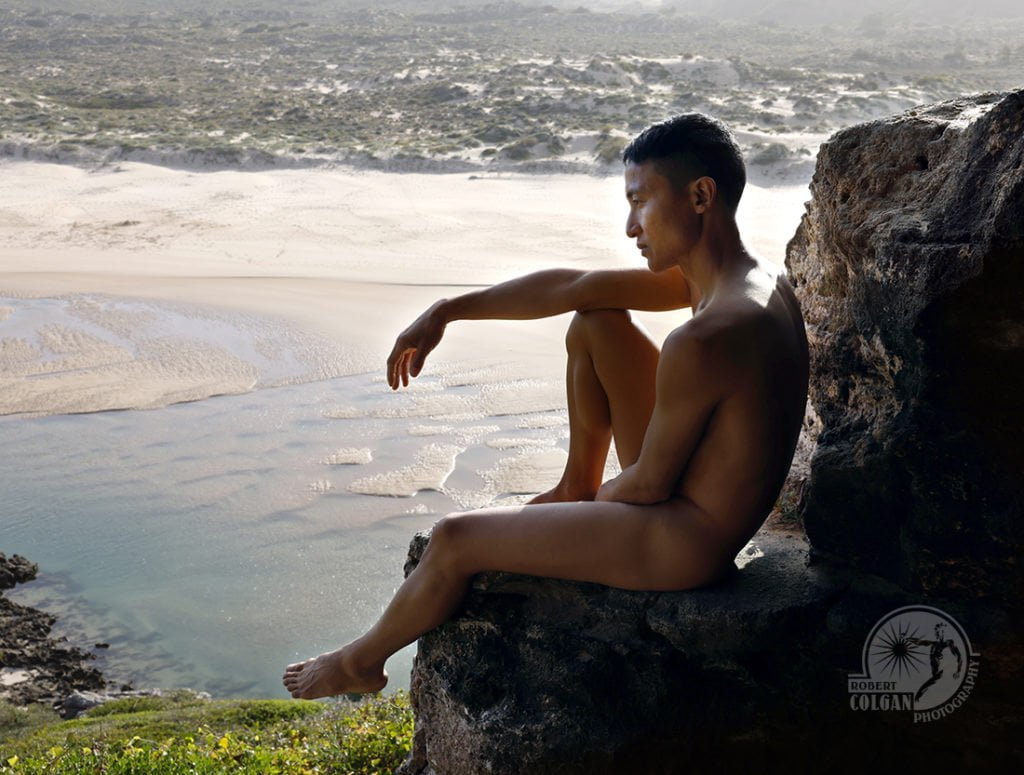 nude man sitting on rock overlooking river