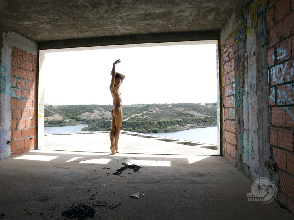 nude man dances in opening of building with countryside in background