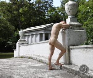 nude man rests beside white bridge with temple in background