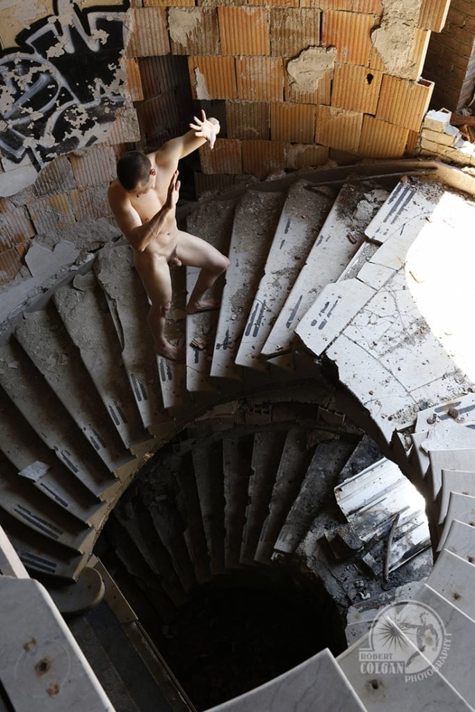 nude man climbs stairs with hands raised to light
