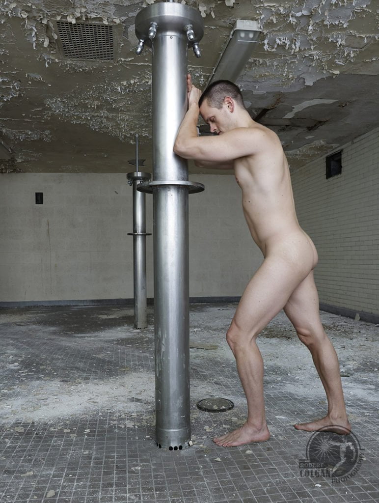 nude man rests beside shower pole in abandoned school