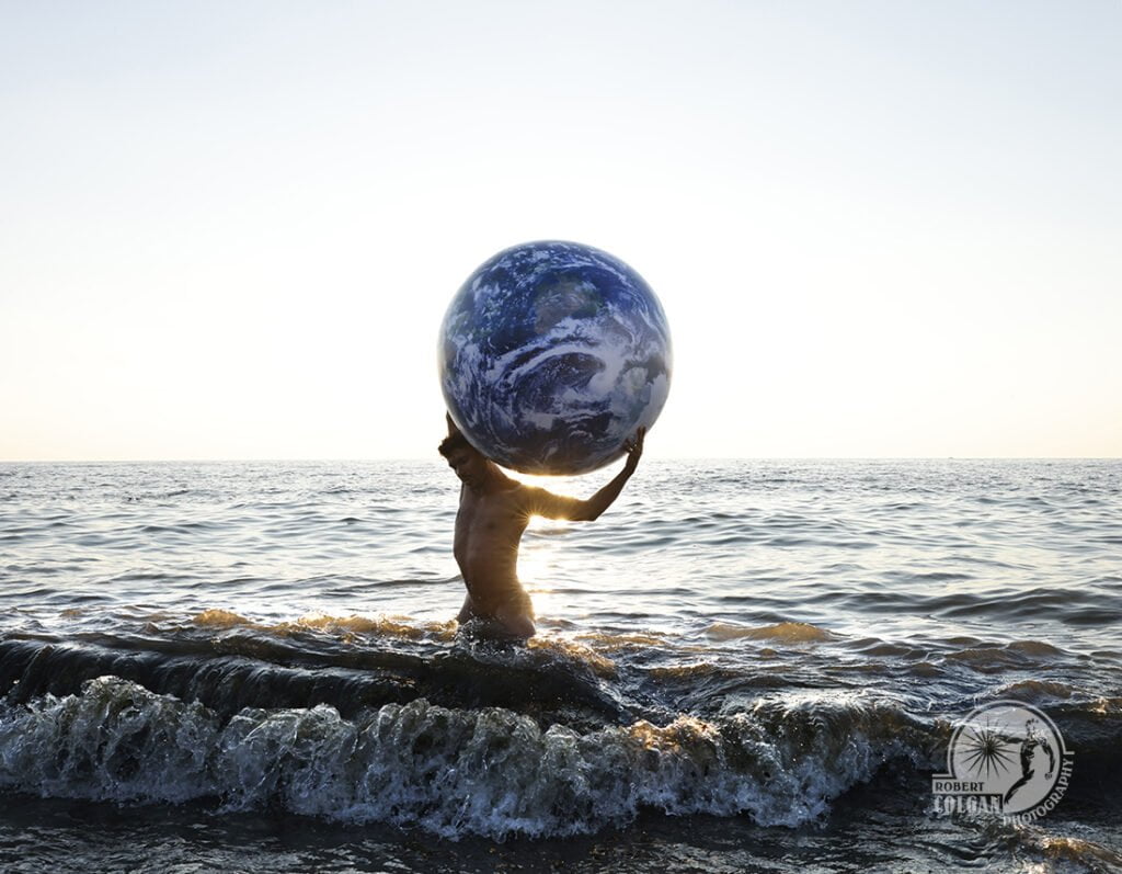 nude man in surf holding planet Earth