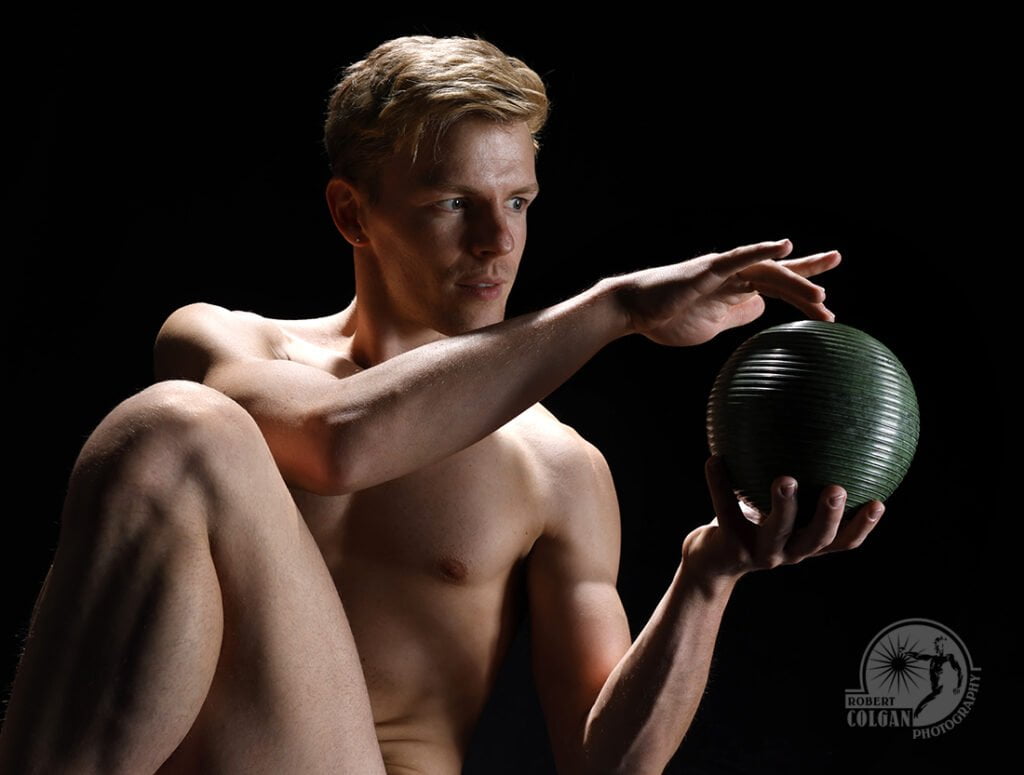 shirtless man in studio lighting holding sphere