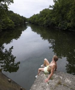 shirtless man sits overlooking river