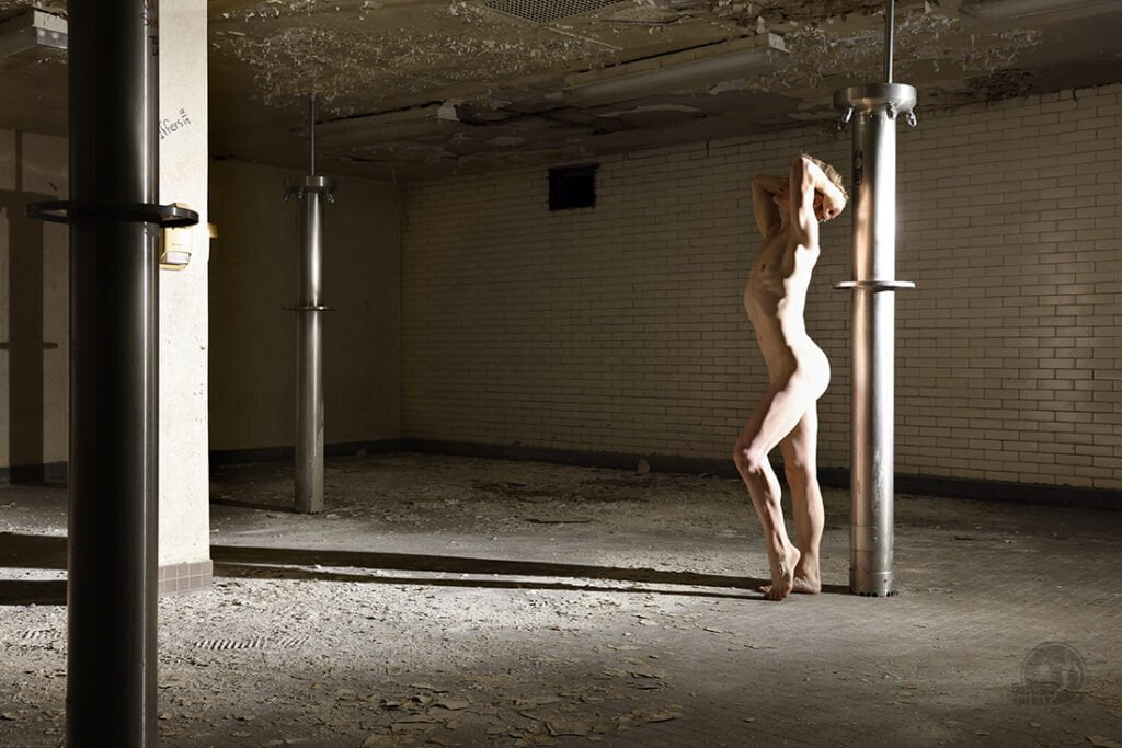 nude man stands in empty shower room