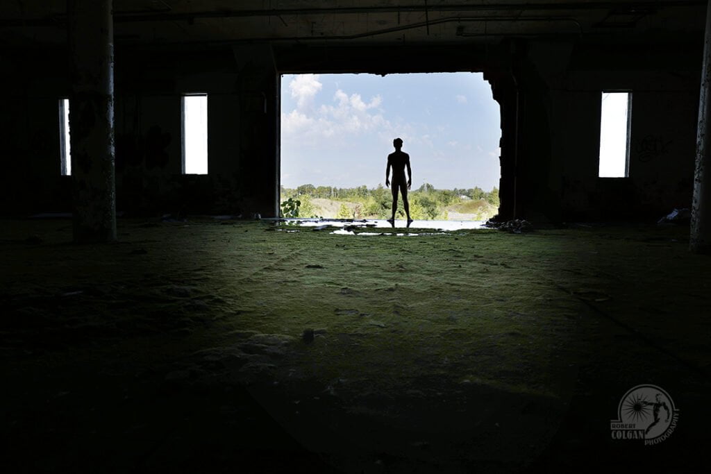 nude man stands in opening of abandoned factory