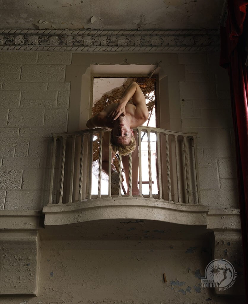 nude man hangs upside over balcony