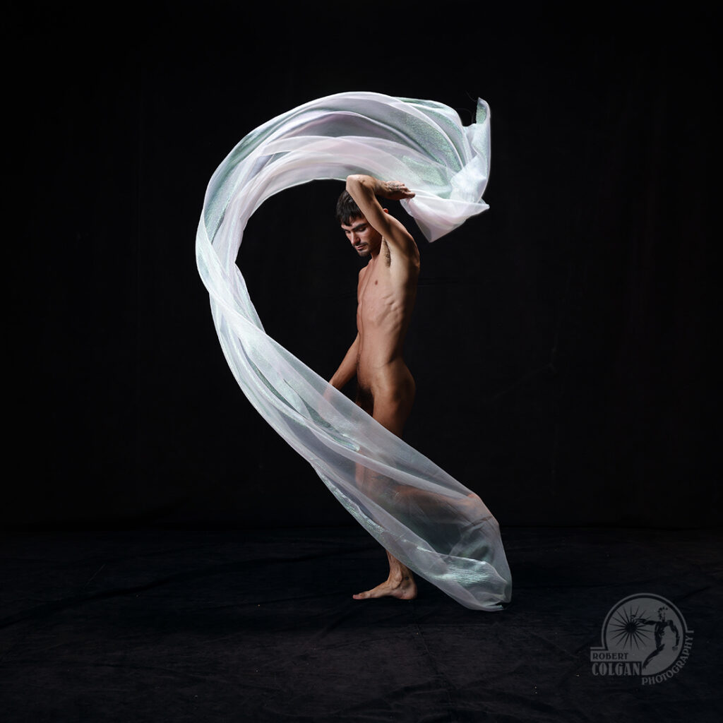 nude man whirls white fabric in studio