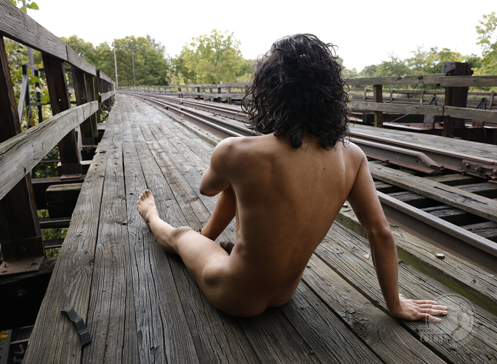 nude man with back to camera facing down railroad tracks