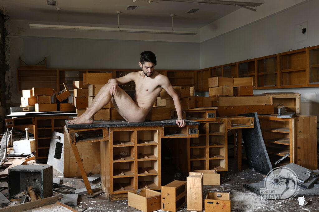 nude man rests on remains of science classroom cabinetry