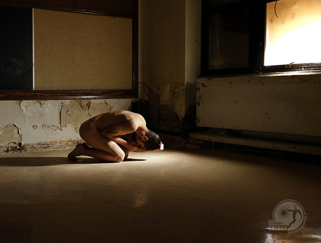 nude man in fetal position on floor of old classroom