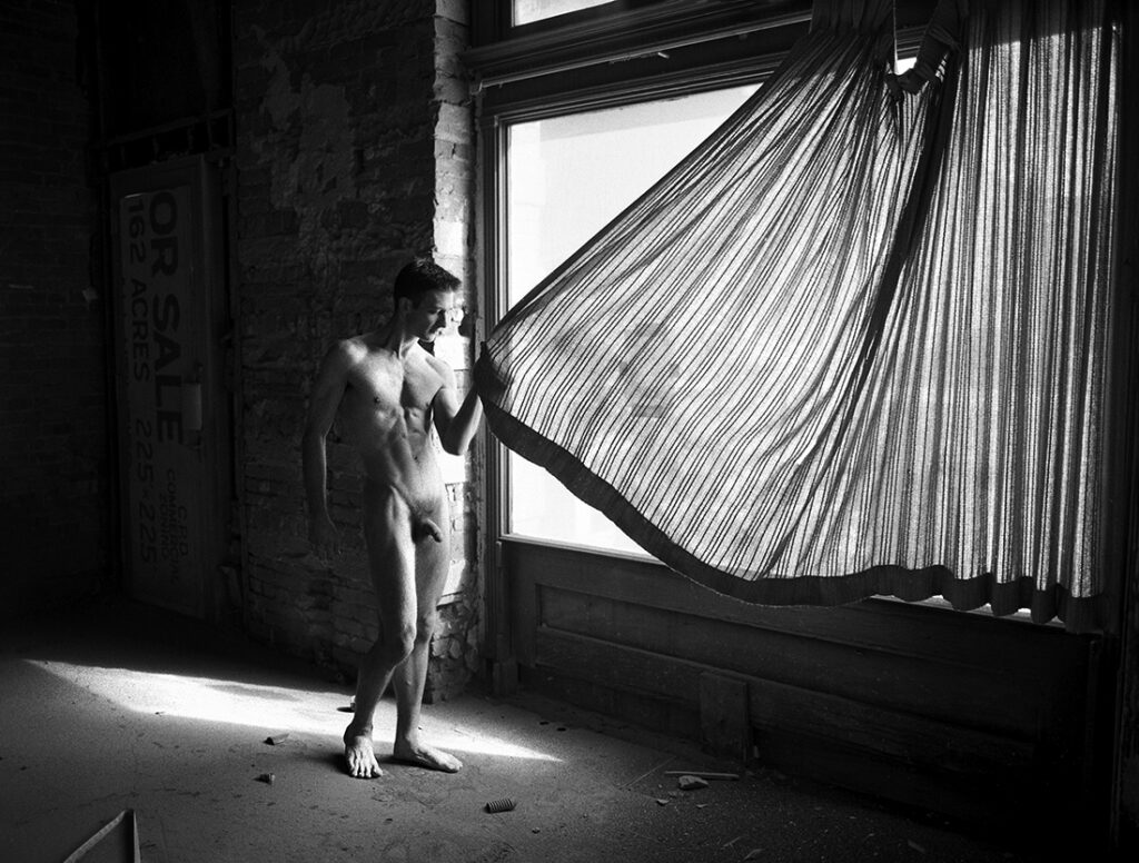 Nude man holds curtain in empty room