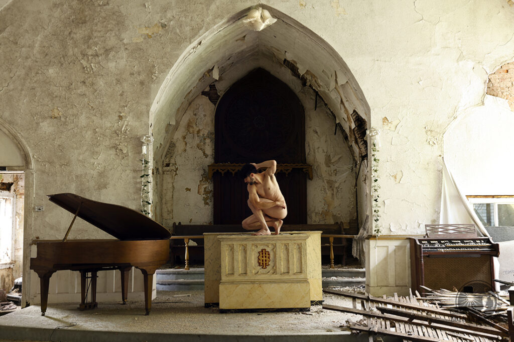nude man crouching on top of altar in decaying church
