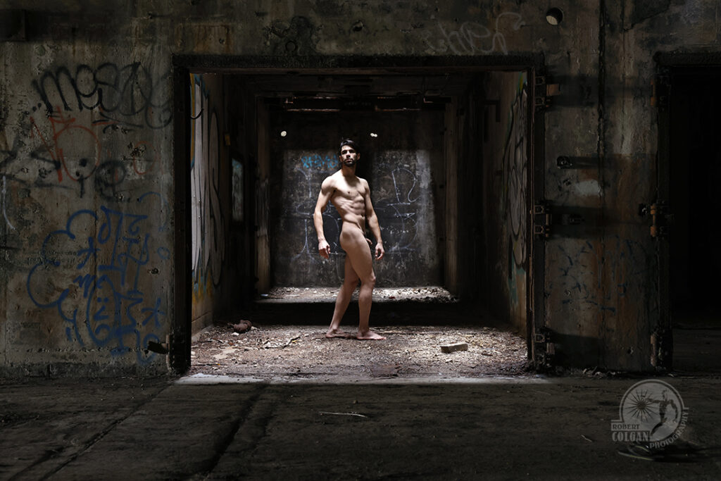 nude man stands in doorway of abandoned industrial building