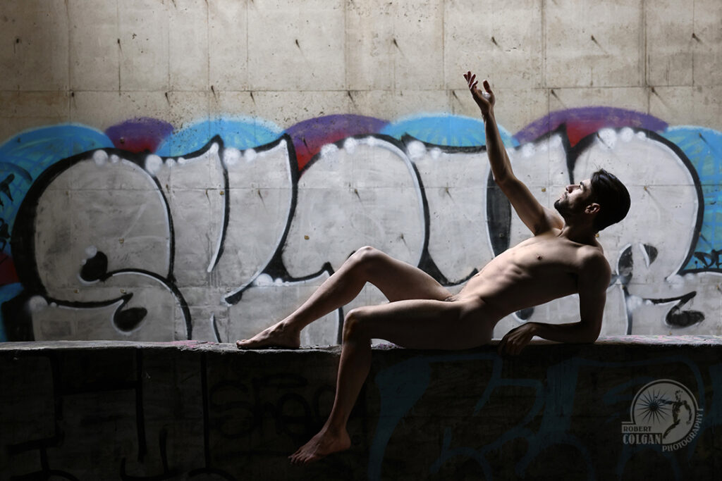 nude man gestures toward opening in ceiling of old factory