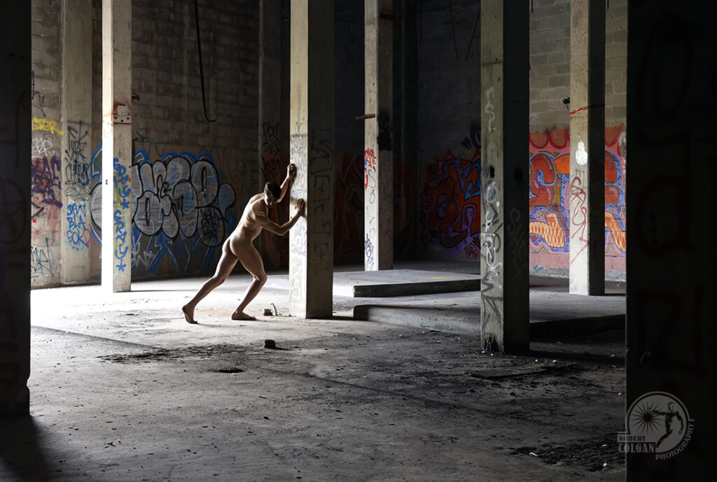 nude man pushes against column in old factory