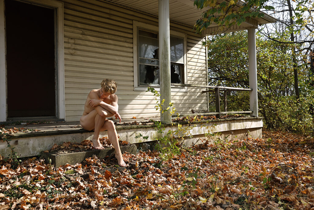 nude man sits on porch of abandoned house