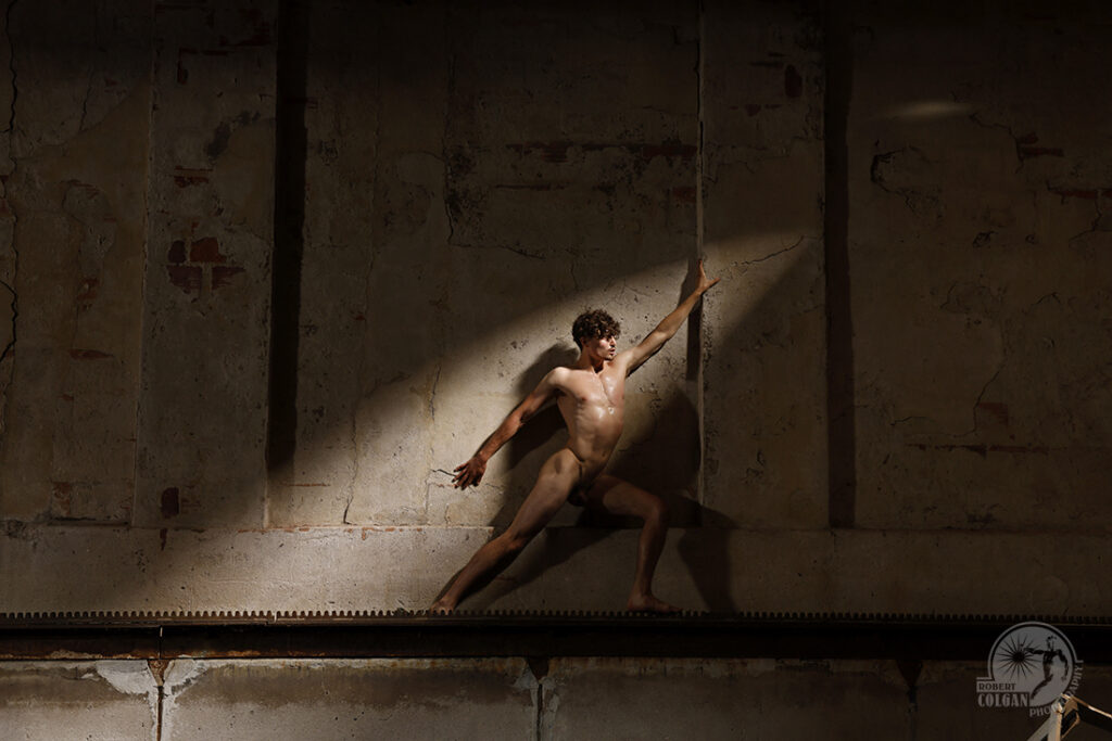 nude man stretches into beam of light from old factory roof