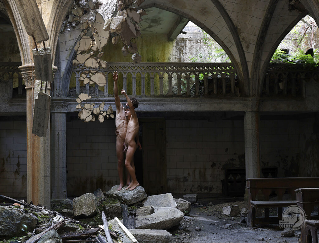 two nude men in derelict church standing on boulder gesturing toward the light in the ceiling