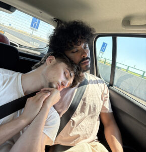two guys sleep in the back seat of a car