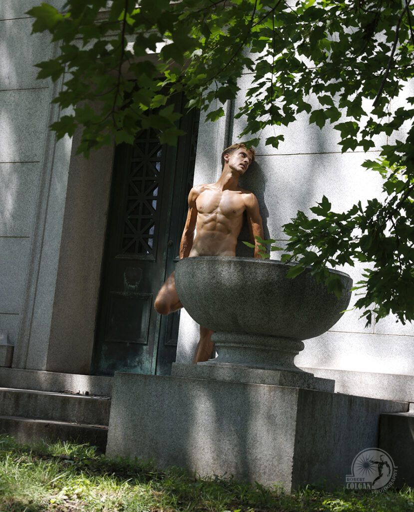 nude man standing against granite tomb