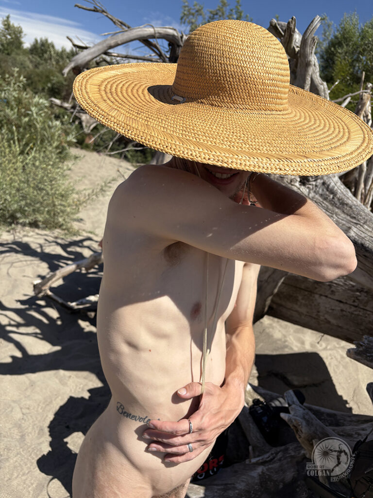 nude man with big wicker hat blocking his face