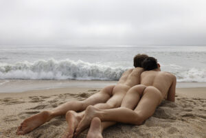 two nude men on a beach looking out over the foggy seas