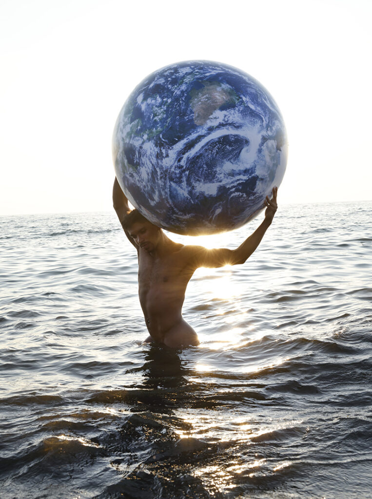 nude man in surf holding planet Earth