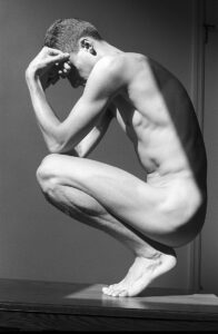 monochrome nude male photographed from the side in a crouching position