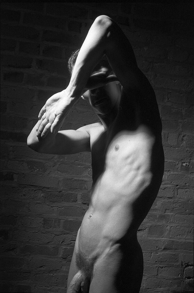 monochrome male nude standing with arms akimbo in a protective pose