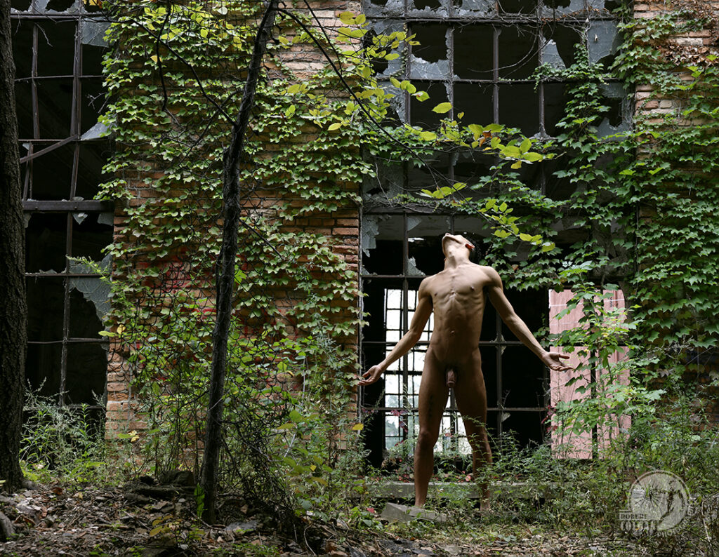 naked man with open arms and head thrown back toward the light coming down the side of an ivy-encrusted building