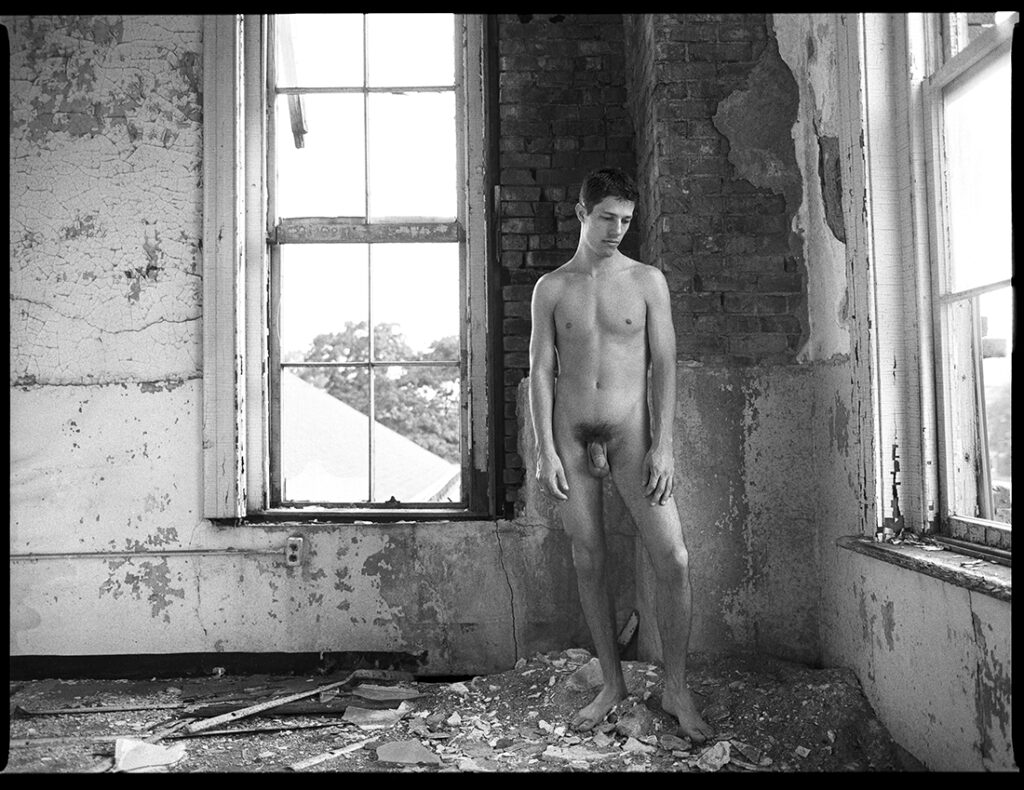 nude man stands dejectedly in ruins of old building