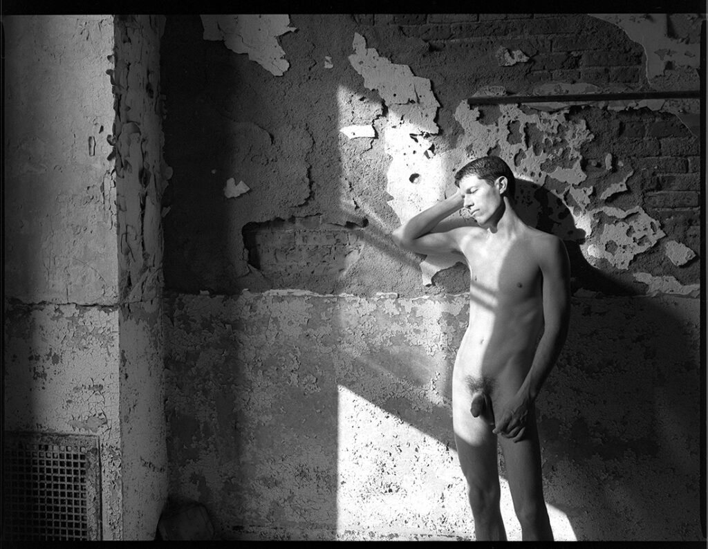 nude man in sun beams in old abandoned building beside crumbling plaster