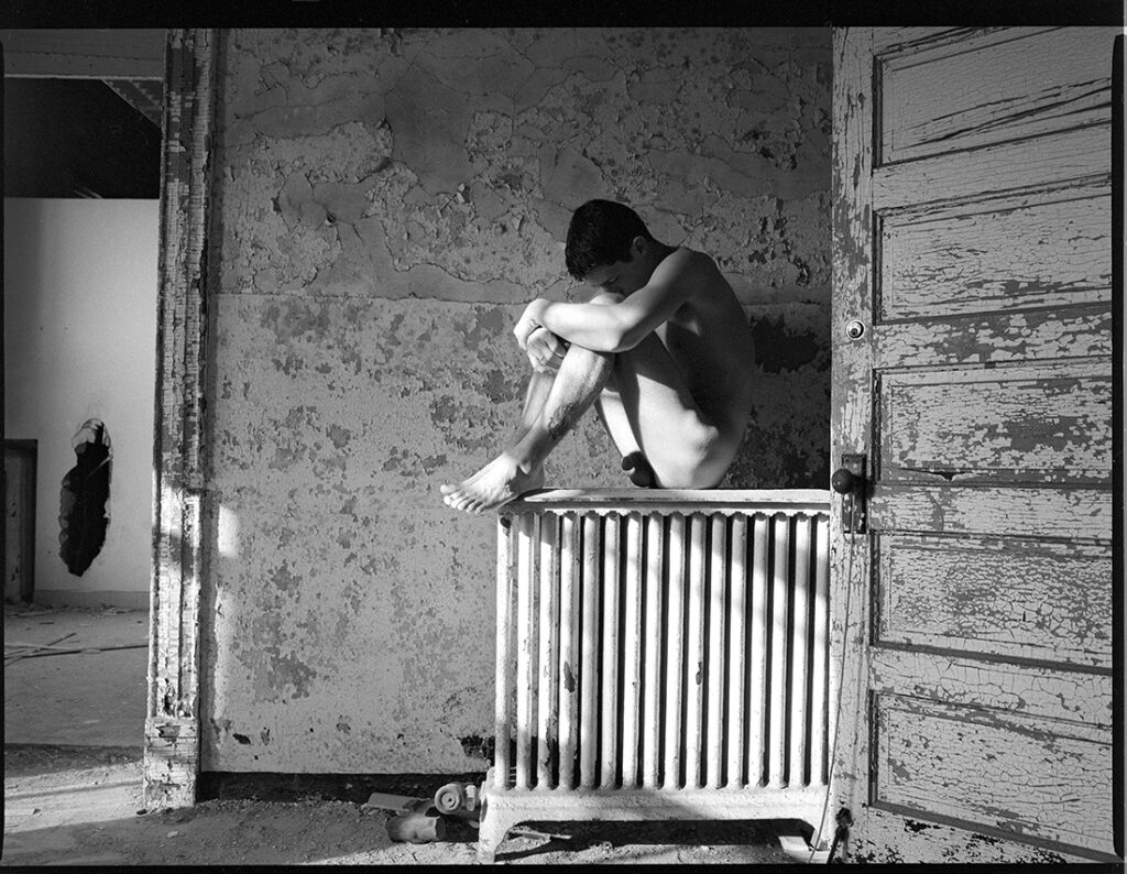 nude man sits on radiator in old building