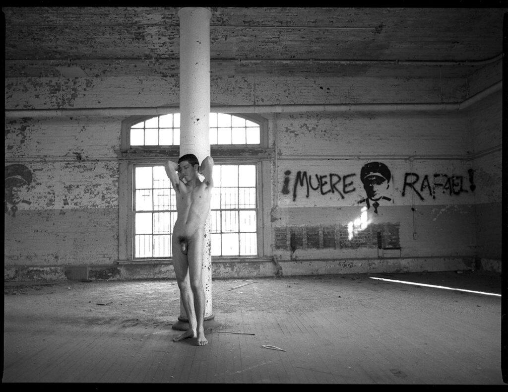 nude man stands against column in empty building