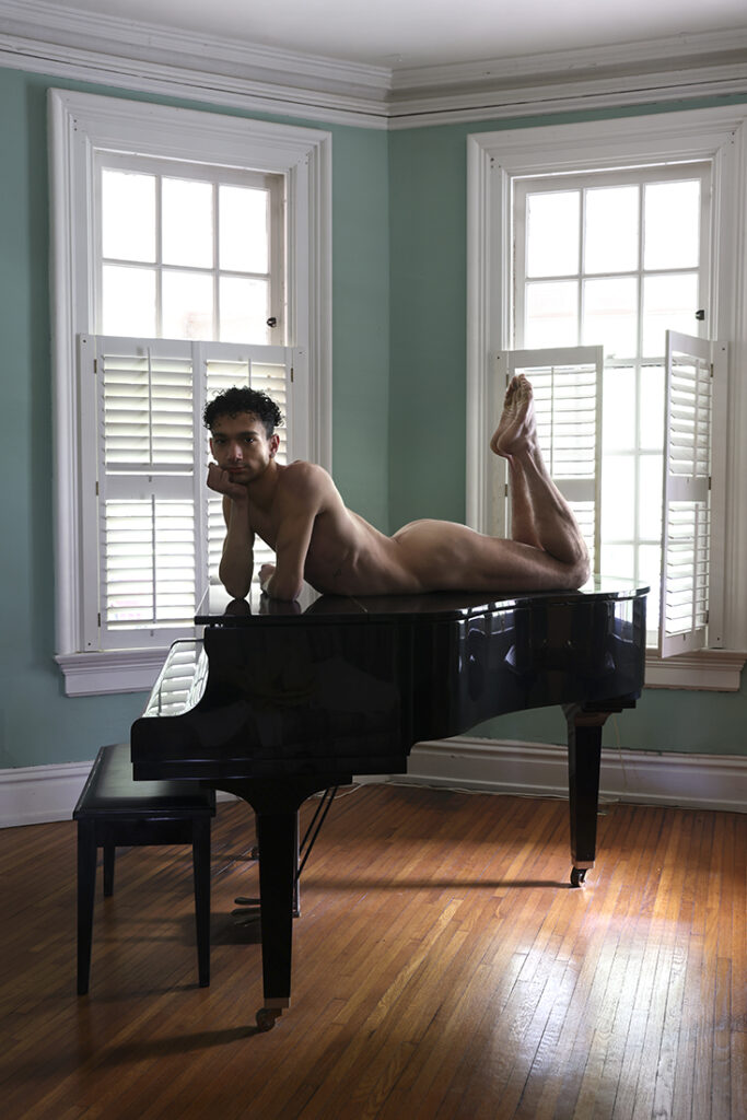 nude man lays on top off black grand piano