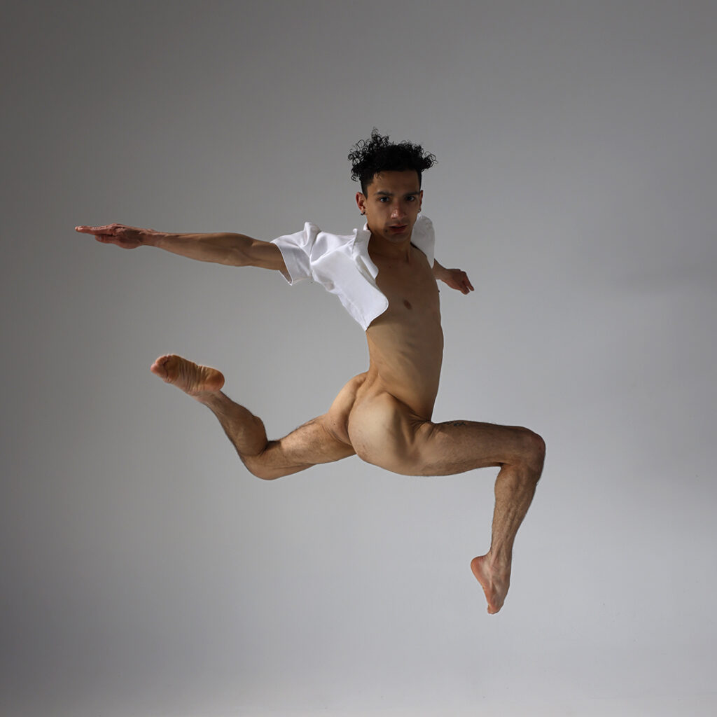 nude dancer leaping in air while extending his leg and arm