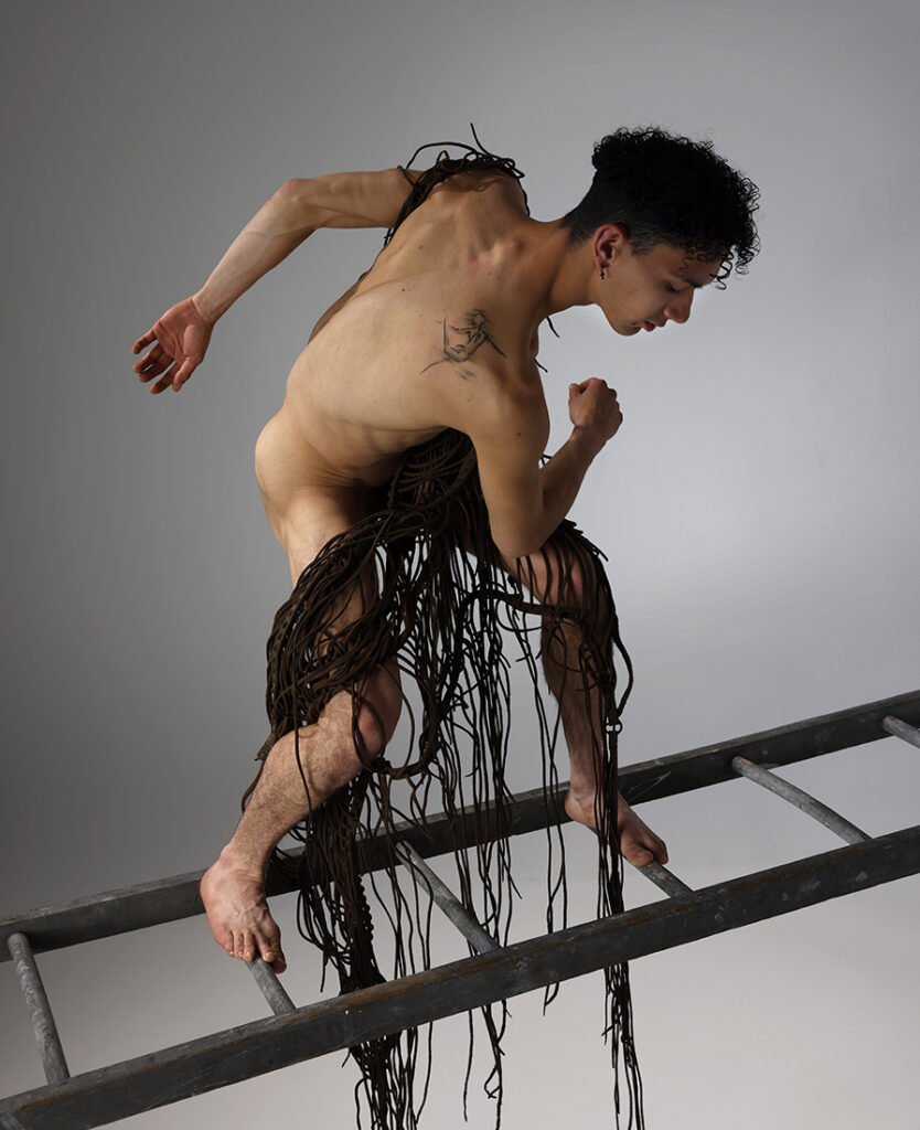 nude man with leather stringed garment in twisted pose on ladder