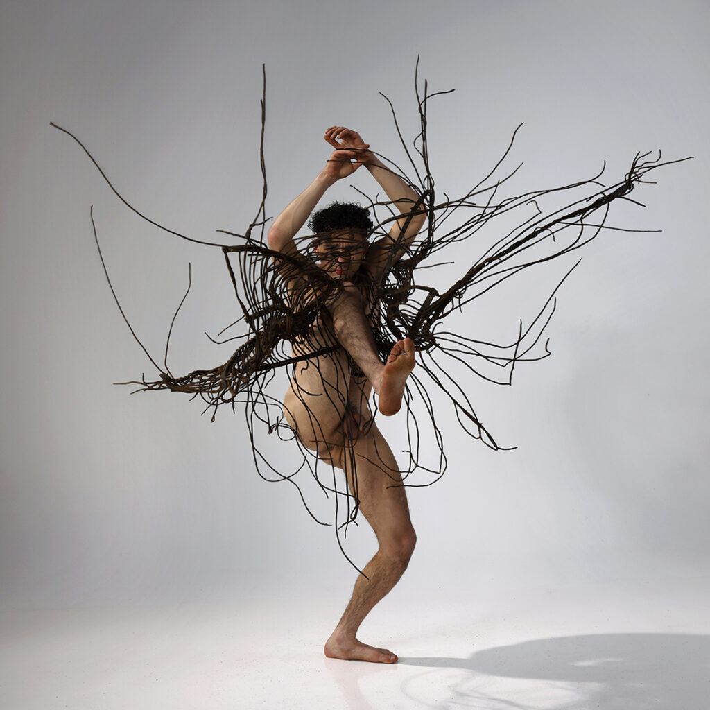 nude man in explosive dance gesture with leather decorative piece flying into the air