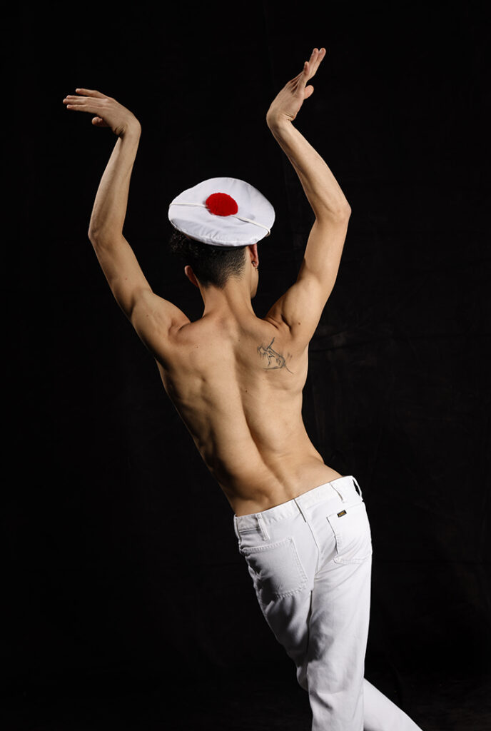 shirtless man with back to camera makes expressive gesture with his hands in air