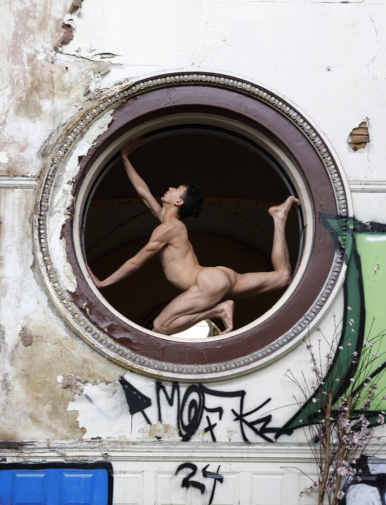 nude man extends his body with arched back into circular window opening