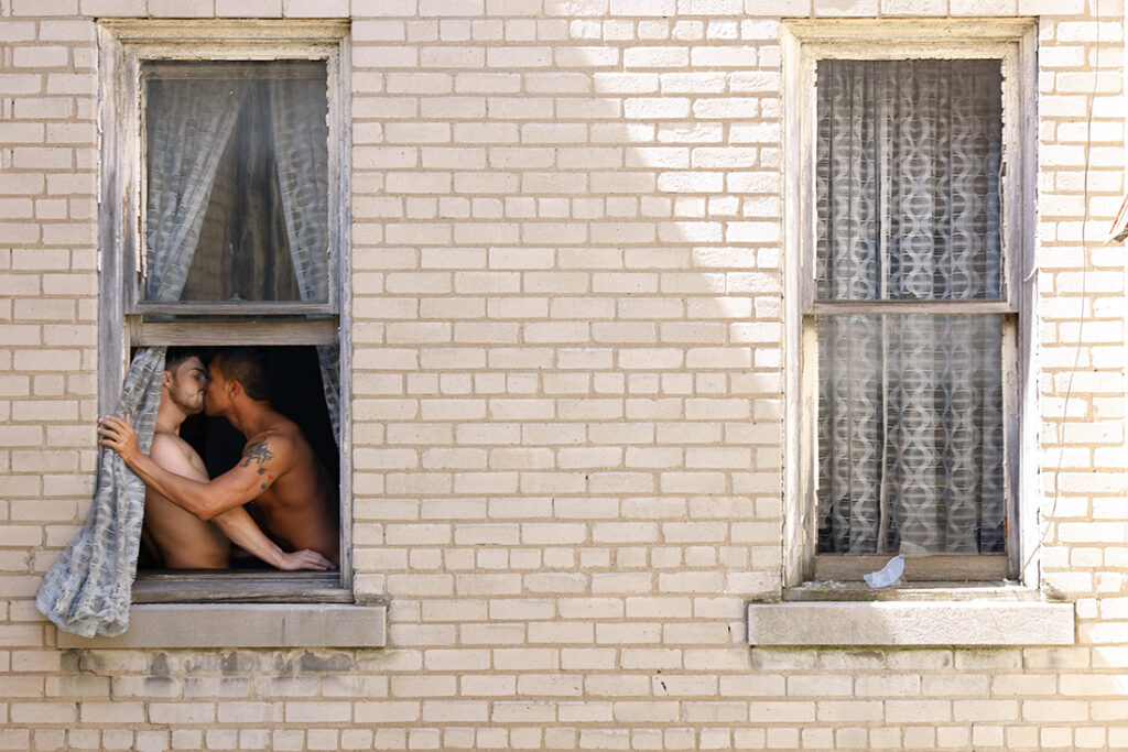 Two men kiss in window opening of apartment building